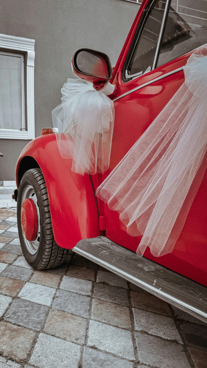 A vintage red car decorated with white tulle for a wedding